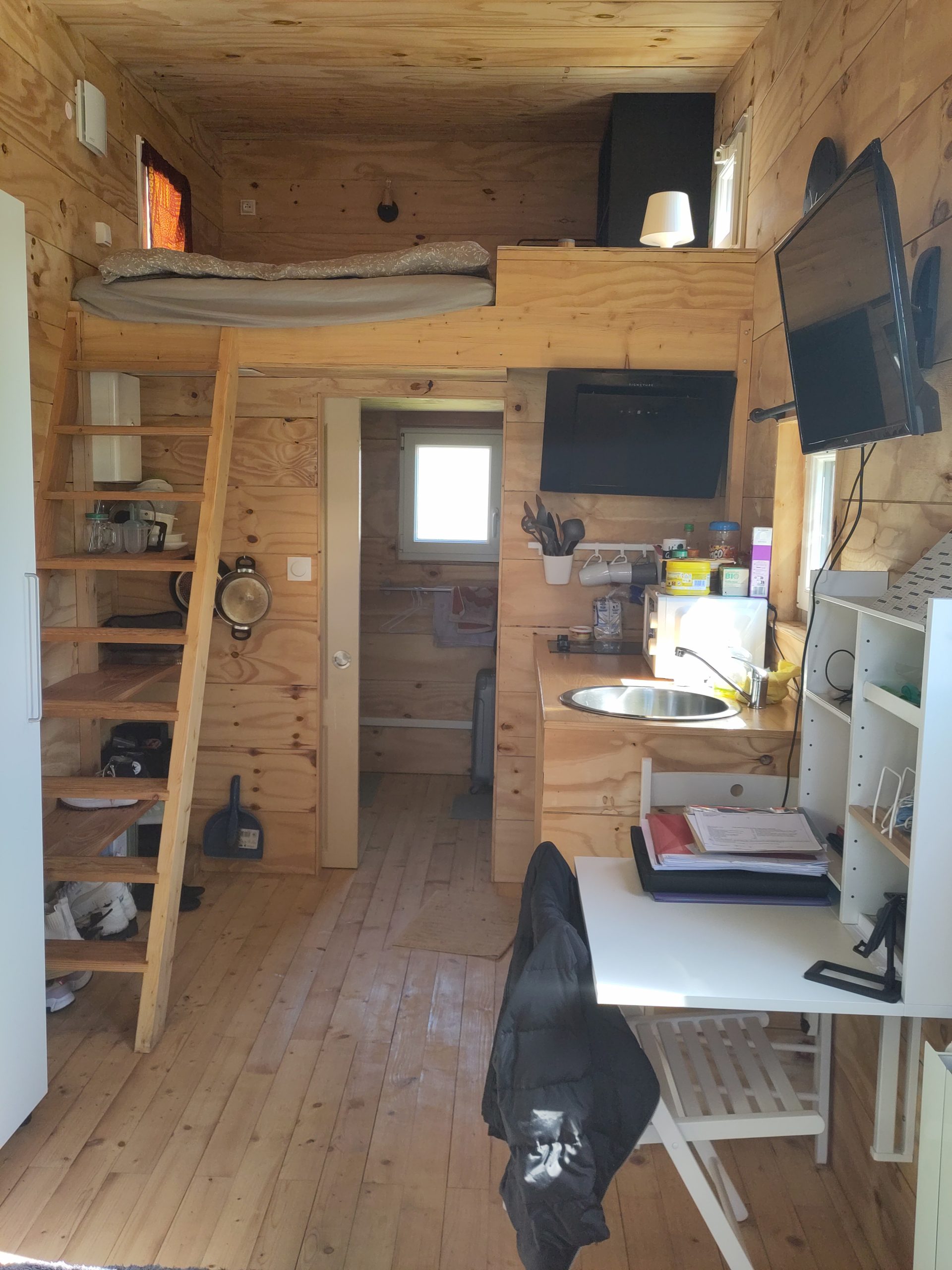 Intérieur d'une tiny house, avec un lit en mezzanine, une table et au fond une salle de bain